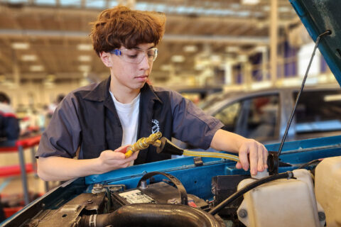 Student working under hood of car