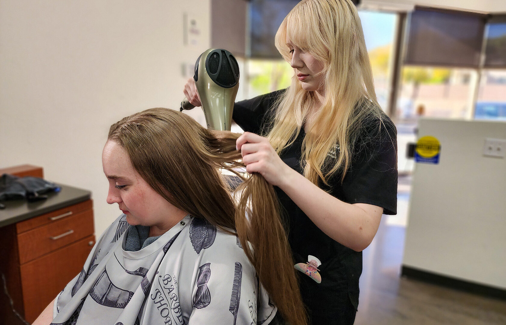 Cosmetology student blow drying client's hair