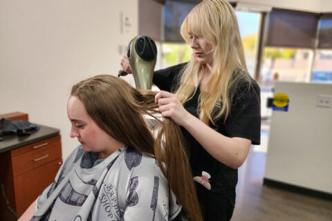 Cosmetology student blow drying client's hair