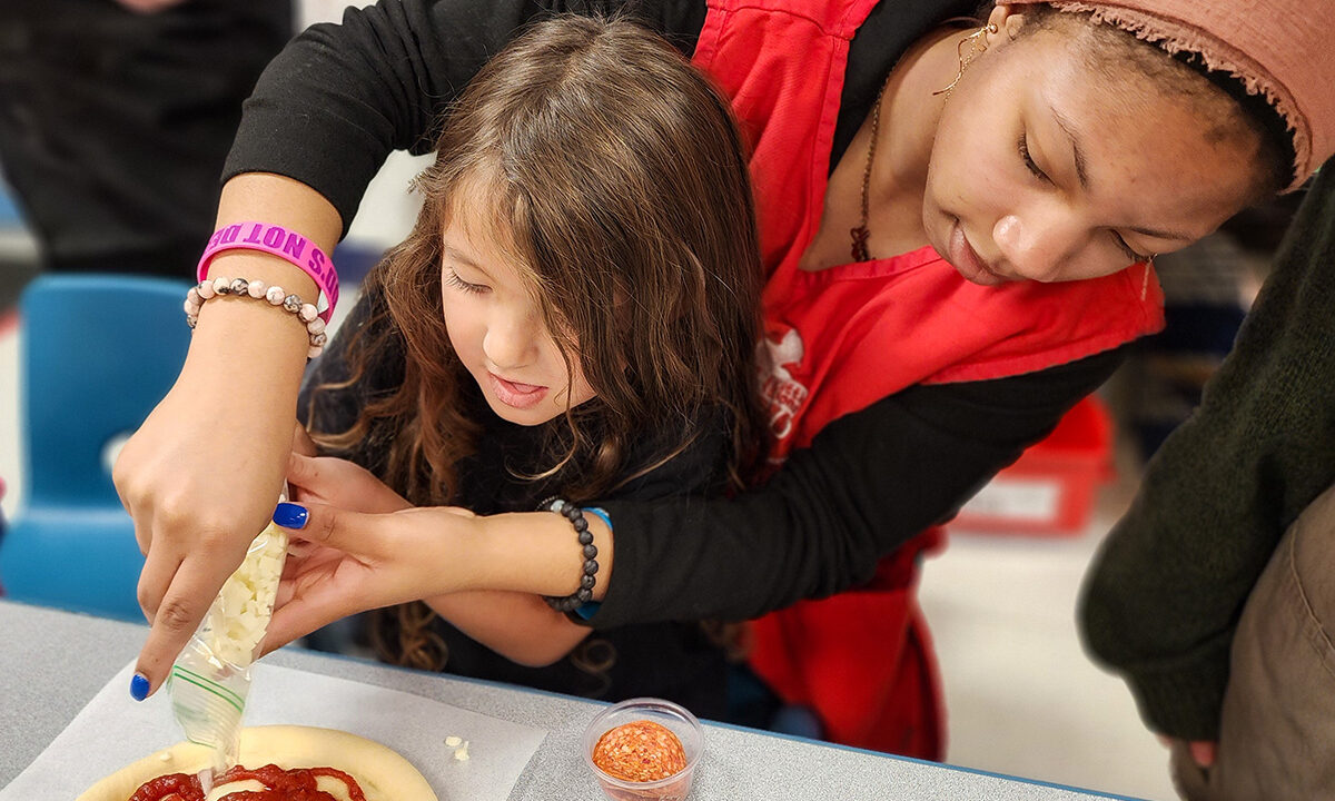 Student helping preschooler make pizza