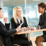 Photo of successful employees gathered around table explaining their ideas in office