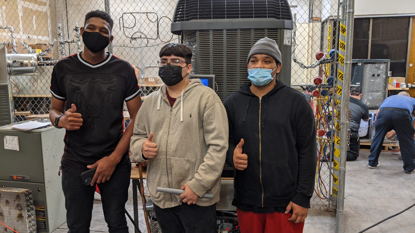 three h v a c students standing in front of their built air conditioner