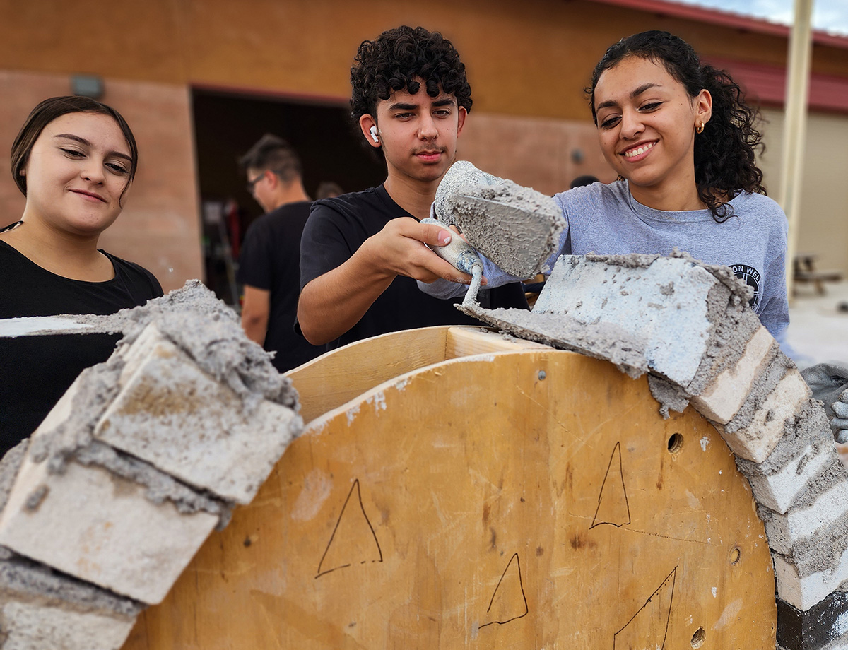 Three students building a concrete arch using masonry skills