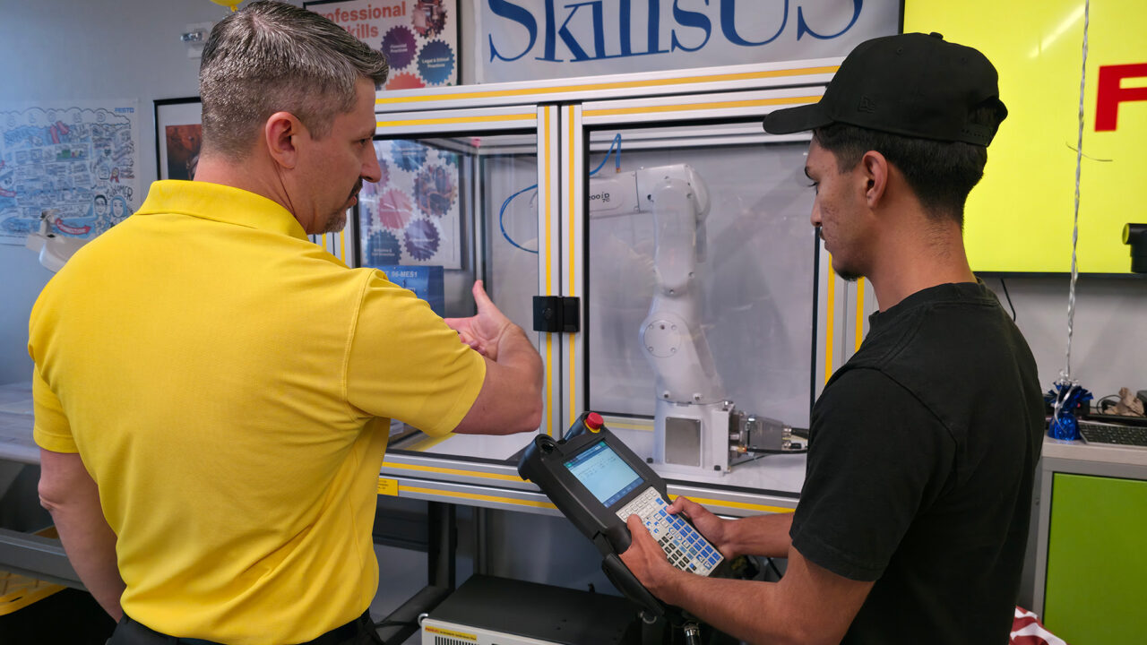 FANUC rep showing student how to use robotic arm